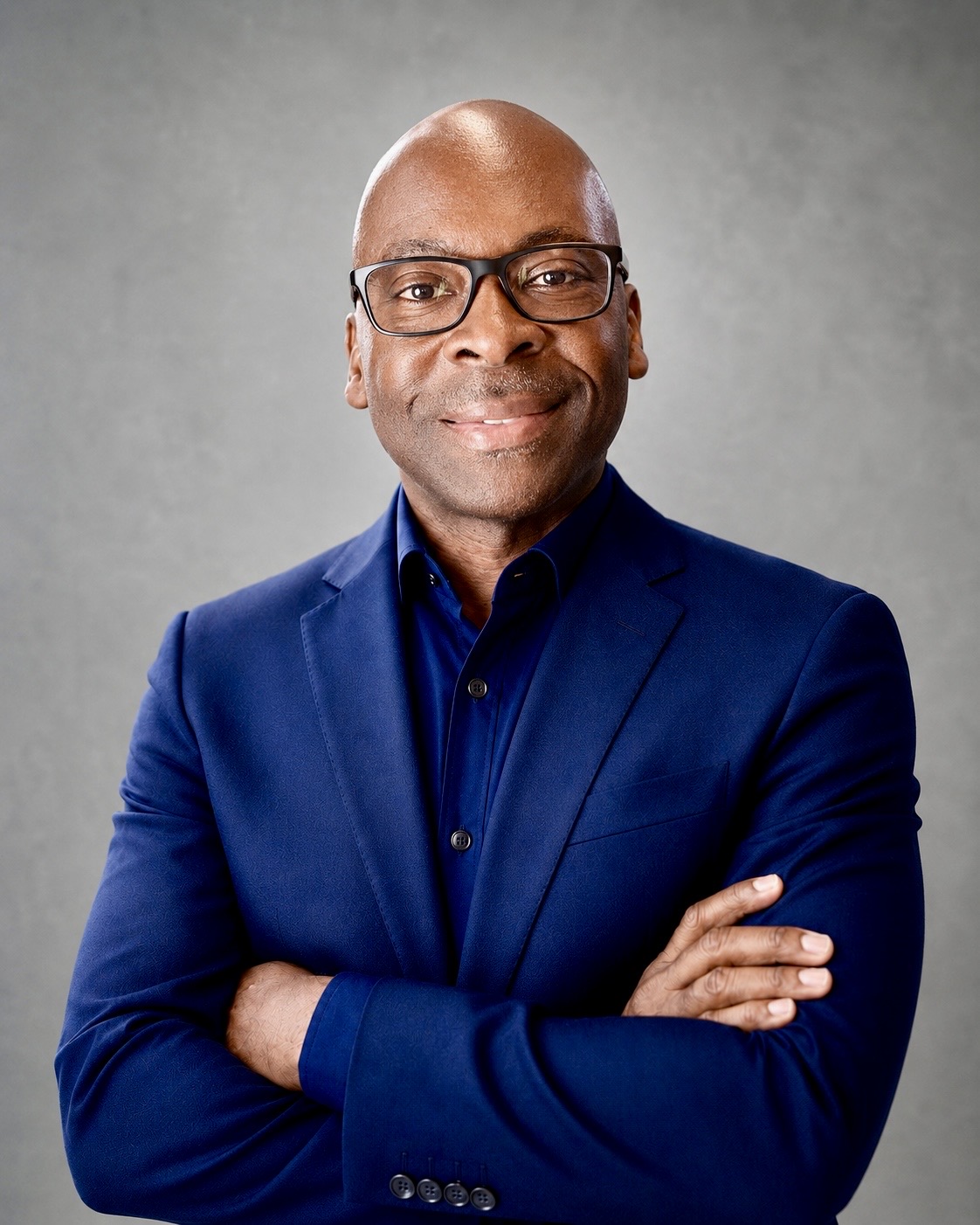 Sammie Cooper, wearing glasses and a blue suit, arms crossed.